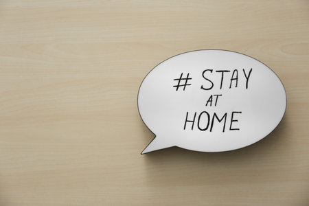 Top view of speech bubble with hashtag STAY AT HOME on wooden background, space for text.