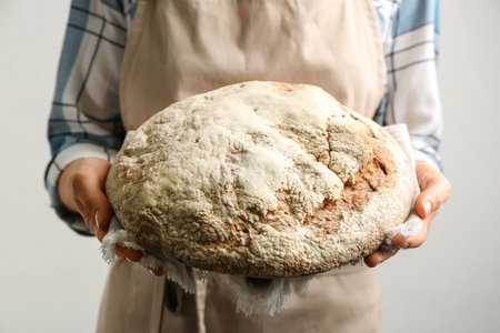 Woman holding freshly baked bread on gray background, closeup