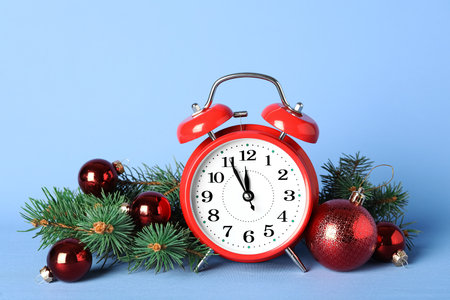 Alarm clock with Christmas decor on light blue background. New Year count down