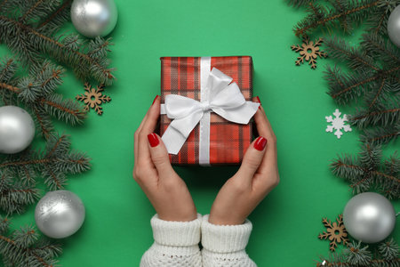 Woman holding gift box near fir tree branches with Christmas decor on green background, top viewの写真素材