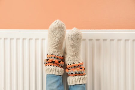 Woman warming legs on heating radiator near color wall, closeup