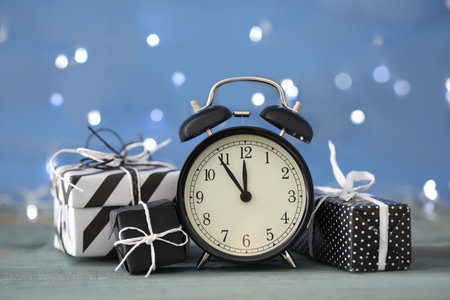 Vintage alarm clock with decor on blue wooden table against blurred Christmas lights. New Year count...