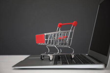 internet shopping. Laptop with small cart on table against gray background