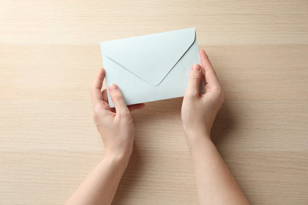 Woman with white paper envelope at wooden table, top view