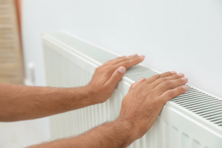 Man warming hands on heating radiator near white wall, closeupの写真素材