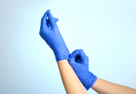 Woman putting on latex gloves against light blue background, closeup of handsの写真素材