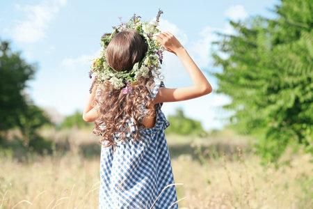 Little girl wearing wreath made of beautiful flowers in the field on sunny dayの写真素材