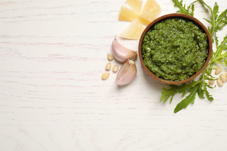Bowl of tasty arugula pesto and ingredients on white wooden table, flat lay. Space for textの写真素材