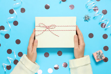 Woman holding Christmas gift on light blue background with decor, top view