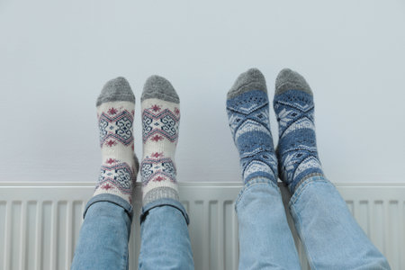 Couple warming legs on heating radiator near white wall, closeupの写真素材