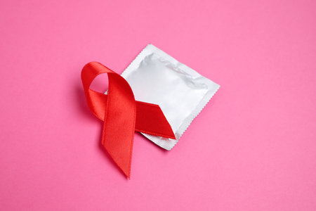 Red ribbon and condom on pink background, closeup. AIDS disease awarenessの写真素材