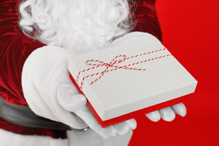 Santa Claus holding Christmas gift on red background, closeupの写真素材