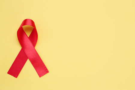 Top view of red ribbon on yellow background, space for text. AIDS disease awarenessの写真素材