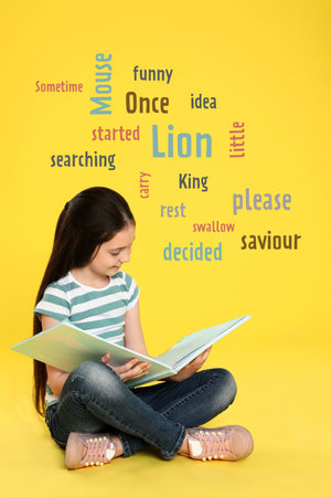 Cute little girl reading book on yellow background with word cloudの写真素材
