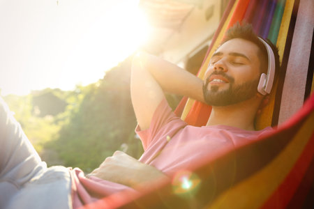Young man listening to music in hammock near motorhome outdoors on sunny dayの写真素材
