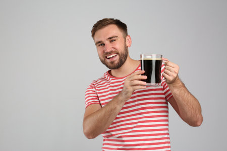 Handsome man with cold kvass on light gray background. Traditional Russian summer drink
