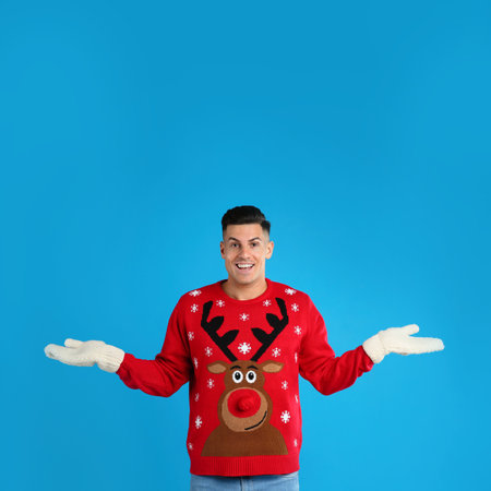 Happy man in Christmas sweater and mittens on blue backgroundの写真素材
