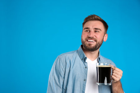 Handsome man with cold kvass on blue background. Traditional Russian summer drinkの写真素材