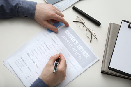 Man filling in driver's license application form at white table, top viewの写真素材
