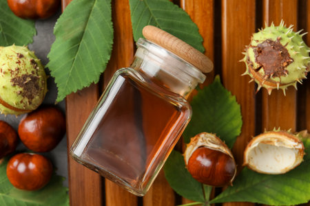 Chestnuts, leaves and jar of essential oil on wooden table, flat layの写真素材