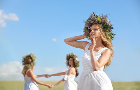 Young women wearing wreaths made of beautiful flowers in the field on sunny dayの写真素材