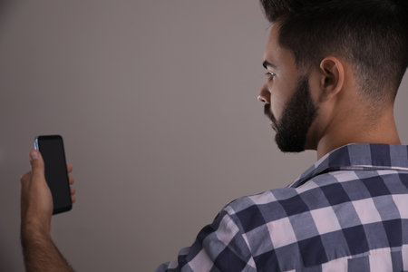 Young man unlocking smartphone with facial scanner on beige background. biometric verificationの写真素材