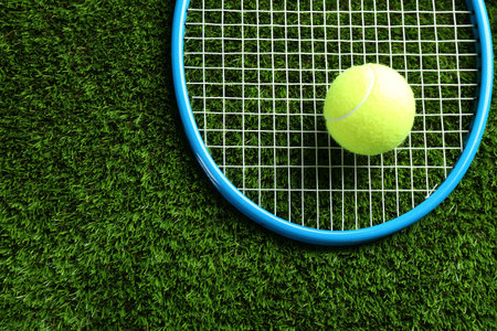 Tennis racket and ball on green grass, top view. Space for text