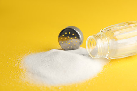 Scattered salt and shaker on yellow background, closeupの写真素材