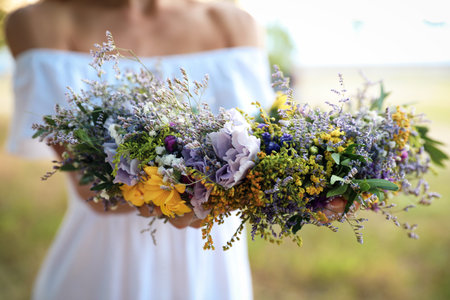 Young woman holding wreath made of beautiful flowers outdoors on sunny day, closeupの写真素材