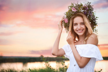 Young woman wearing wreath made of beautiful flowers outdoors at sunsetの写真素材
