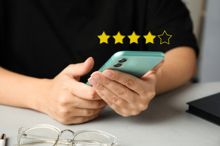 Woman leaving review online via smartphone at table, closeup. Four out of five stars over gadget