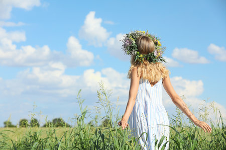 Young woman wearing wreath made of flowers in field on sunny day, back viewの写真素材