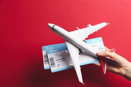 Woman holding toy airplane and tickets on red background, closeup