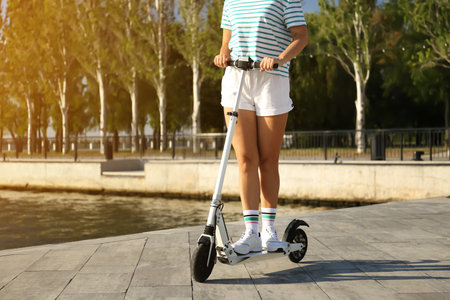 Young woman riding modern kick scooter along waterfront, closeupの写真素材