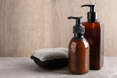 Dispenser bottles with water drops and bast wisp on beige marble table, space for text. men's cosmeticsの写真素材