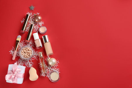 Christmas tree shape of decorative cosmetic products on red background, flat lay with space for text. winter careの写真素材