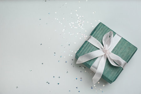 Blue gift box and shiny confetti on light background, top view. Space for text