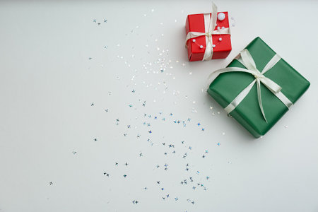 Christmas gift boxes with shiny confetti on light background, flat lay. Space for text
