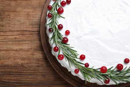 Traditional Christmas cake decorated with rosemary and cranberries on wooden table, top viewの写真素材