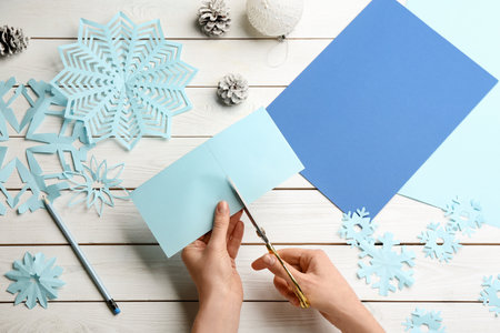 Woman making paper snowflake at white wooden table, top viewの写真素材