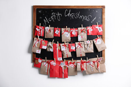 Blackboard with Christmas advent calendar on white wall indoors