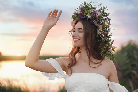Young woman wearing wreath made of beautiful flowers outdoors at sunsetの写真素材