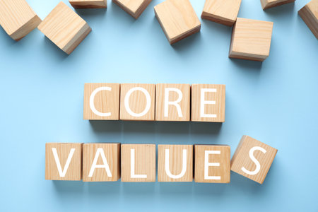 Wooden cubes with phrase CORE VALUES on light blue background, flat lay