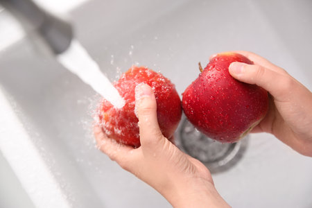 Woman washing fresh red apples in kitchen sink, top viewの写真素材
