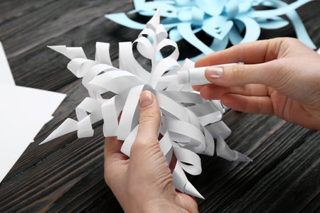 Woman making paper snowflake at black wooden table, closeupの写真素材