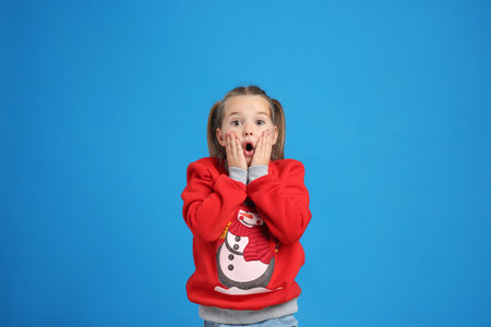 Surprised little girl in Christmas sweater on blue backgroundの写真素材