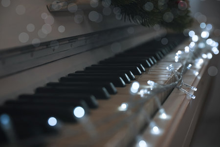Glowing fairy lights on piano keys indoors, closeup. Christmas music