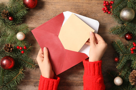 Woman taking blank Christmas card from envelope at wooden table, top view with space for textの写真素材