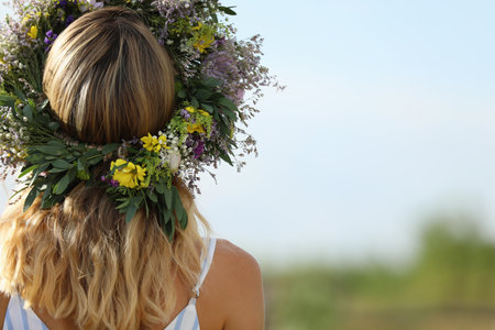 Young woman wearing wreath made of beautiful flowers outdoors on sunny day, back viewの写真素材