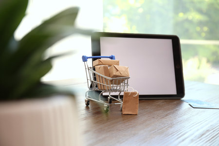 internet shopping. Small cart with boxes and bag near modern tablet on wooden table indoorsの写真素材